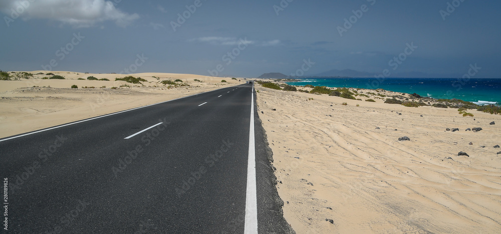 Natural landscape with amazing dunes and asphalt road in Fuerteventura, Natural park Corralejo, Canary Island Spain. Summer exotic vacation postcard from a tropical island in the ocean. Panorama view