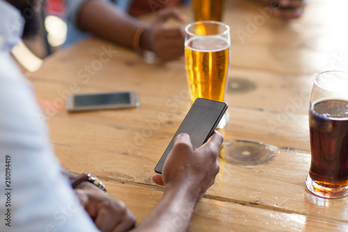 people and technology concept - man with smartphone drinking beer and reading message at bar or pub