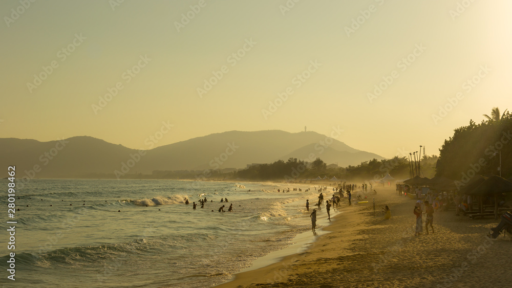 Tropical beach, people having fun in the sea, the golden twilight of sunset light. Soft focus. Tropical beach, people having fun in the sea, the golden twilight of sunset light. Soft focus.