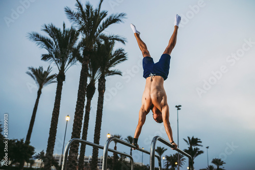 fitness, sport, training, calisthenics and lifestyle concept - young man performing Handstand on parallels bar