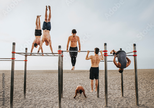 fitness, sport, training, calisthenics and lifestyle concept - Group of guys training on the beach workout bars photo