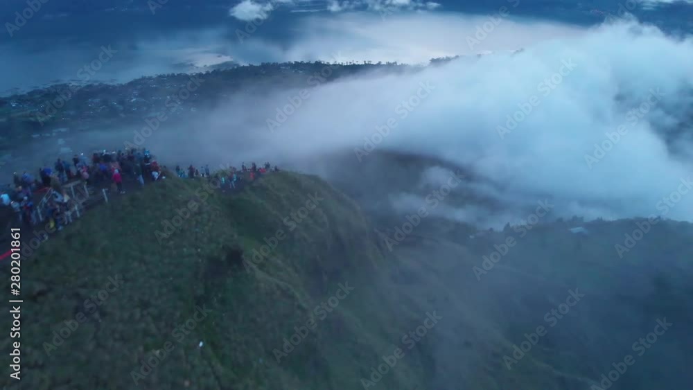 Tourists line the rim of Mount Batur for a sunrise view of the volcano known for double calderas. Aerial view from drone as sun breaks through clouds. Tourists line the rim of Mount Batur for a sunrise view of the volcano known for double calderas. Aerial view from drone as sun breaks through clouds.