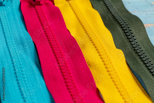 Pack a lot of colorful plastic zippers stripes with sliders pattern for handmade sewing tailoring on the blue denim background close up selective focus