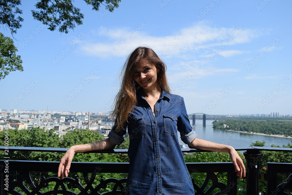 Young brunette girl in denim clothes standing on the bridge on the background of the city. Young brunette girl in denim clothes standing on the bridge on the background of the city.