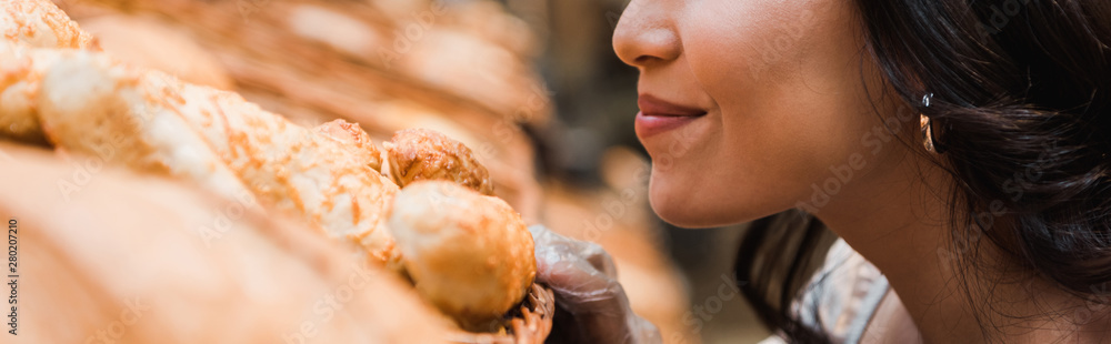 panoramic shot of cheerful woman smiling while smelling bread in supermarket panoramic shot of cheerful woman smiling while smelling bread in supermarket