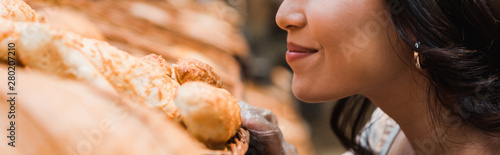 Bild auf Leinwand panoramic shot of cheerful woman smiling while smelling bread in supermarket