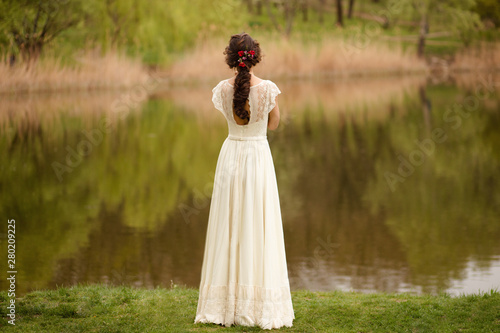 Quadro su tela Rear view of a young anonymous bride in a beautiful full wedding dress, with hairstyle, looking down, nature background