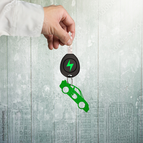 Green energy electric car and Eco-friendly environmental protection concept. Man hand holding electric car key with green leaves keyring in sports car shape, on doodels wall background. photo