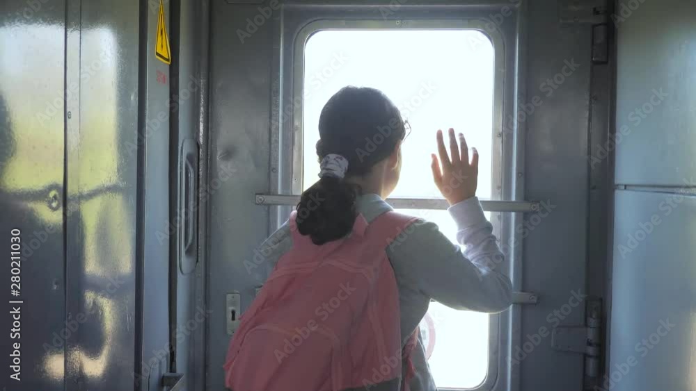 little teenage girl is a backpacker traveling by train. travel transportation railroad concept. tourist school girl in the train wagon with backpack looking out lifestyle the window waving his hand little teenage girl is a backpacker traveling by train. travel transportation railroad concept. tourist school girl in the train wagon with backpack looking out lifestyle the window waving his hand