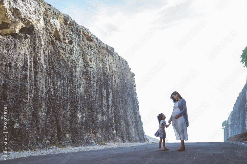 image of pregnant mother stands with her daughter. During the day between cliffs