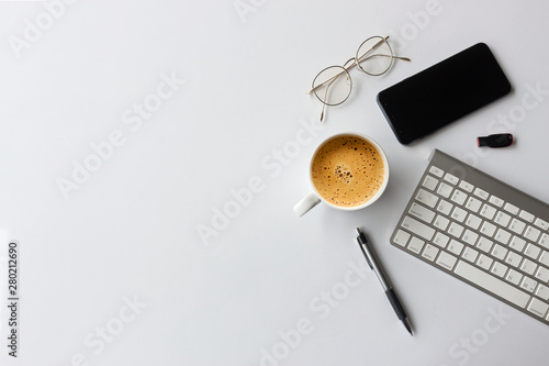 business concept. top view of office desk workspace with smartphone, pen, keyboard, glasses and hot coffee cup on white table background. over light photo