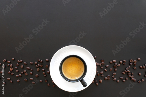 hot espresso and coffee bean on black table with soft-focus and over light in the background. top view