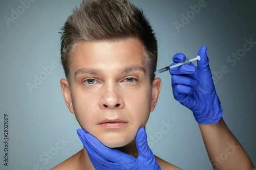 Close-up portrait of young man isolated on grey studio background. Filling surgery procedure. Concept of men's health and beauty, cosmetology, self-care, body and skin care. Anti-aging.