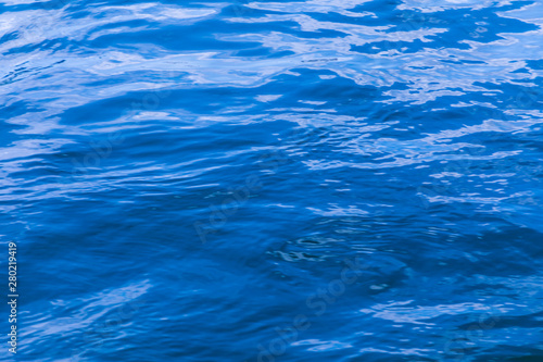 The background or texture of the blue water surface of the river, lake or sea with the waves, ripples and flares