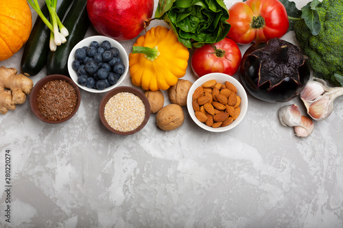 Mix of fresh healthy vegetarian ingredients of vegetables, nuts, seeds, bran, fruit and berries on a gray cement background. Top view, copy space.