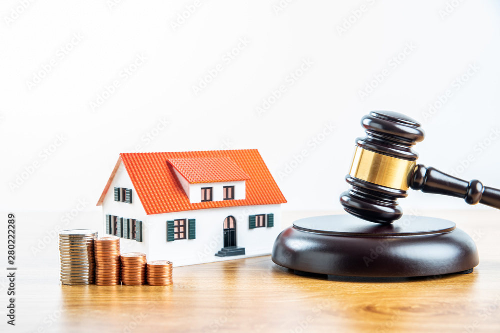 A row of coins on a small house model and a law auction hammer A row of coins on a small house model and a law auction hammer