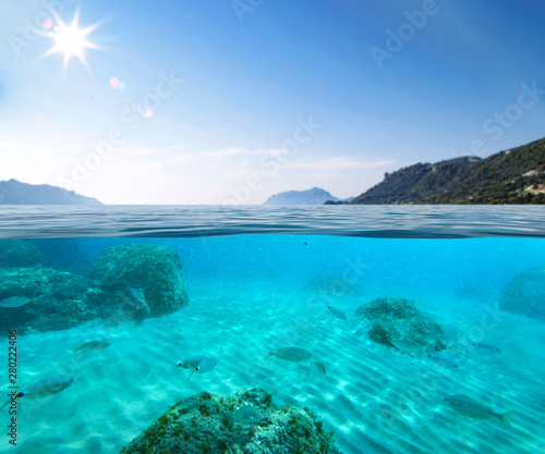 Blue sunny sky, an island in the ocean and underwater sandy rocky sea view.