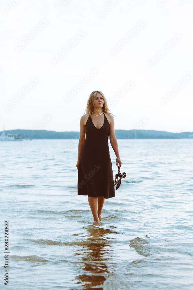 woman in black light dress walking barefoot by sea beach woman in black light dress walking barefoot by sea beach
