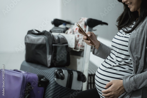 Pregnant Asian women smile while looking at their cellphones while sitting waiting in the airport waiting room