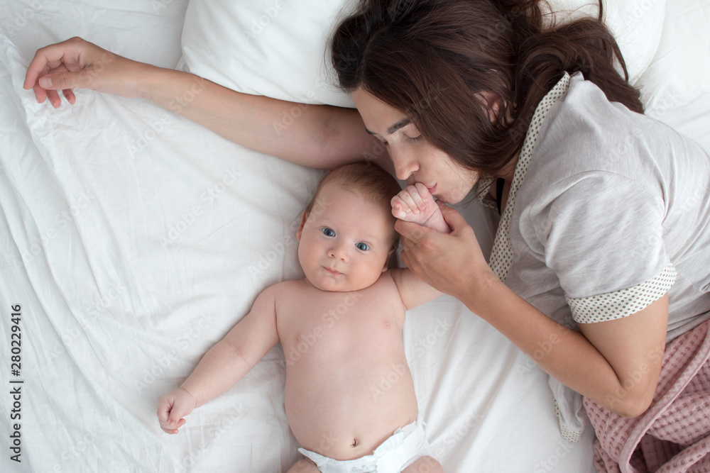 The mother kisses the baby . The brunette lies with a blind child. Top view The mother kisses the baby . The brunette lies with a blind child. Top view
