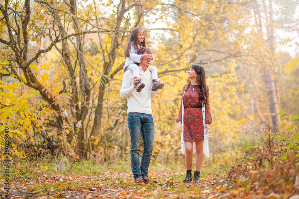 Mom, dad and daughter walk through the autumn forest. Daughter sits on father's shoulders Mom, dad and daughter walk through the autumn forest. Daughter sits on father's shoulders