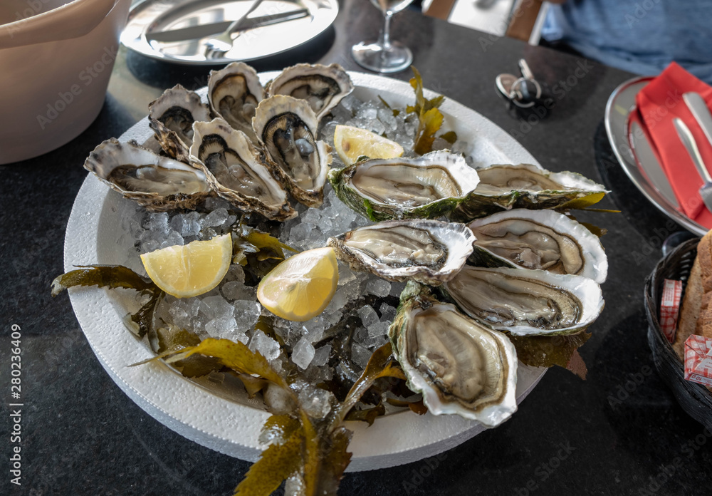 Top view on Fresh oyster with lemon on a plate in the restaurant. Fresh wholesome and healthy seafood, Restaurant delicacy. Serving dish with oysters. Family lunch with wine on an oyster farm. Top view on Fresh oyster with lemon on a plate in the restaurant. Fresh wholesome and healthy seafood, Restaurant delicacy. Serving dish with oysters. Family lunch with wine on an oyster farm.