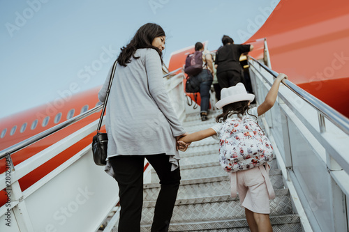 Asian pregnant women and their daughters go up the plane stairs ready for vacation