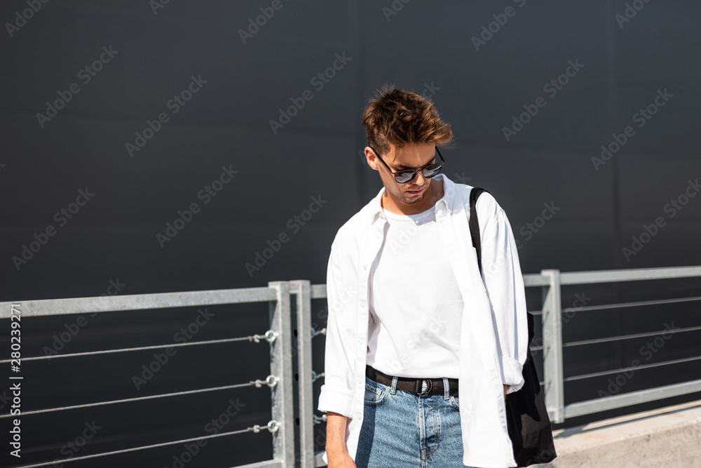 Young model man with hairstyle in stylish white shirt in t-shirt in blue  jeans in