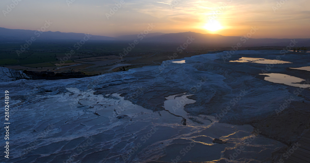 Fototapeta premium Turkey, sunset on the travertine terraces at Pamukkale (Cotton Castle), natural site of sedimentary rock deposited by water from the hot springs, famous for a carbonate mineral left by flowing water