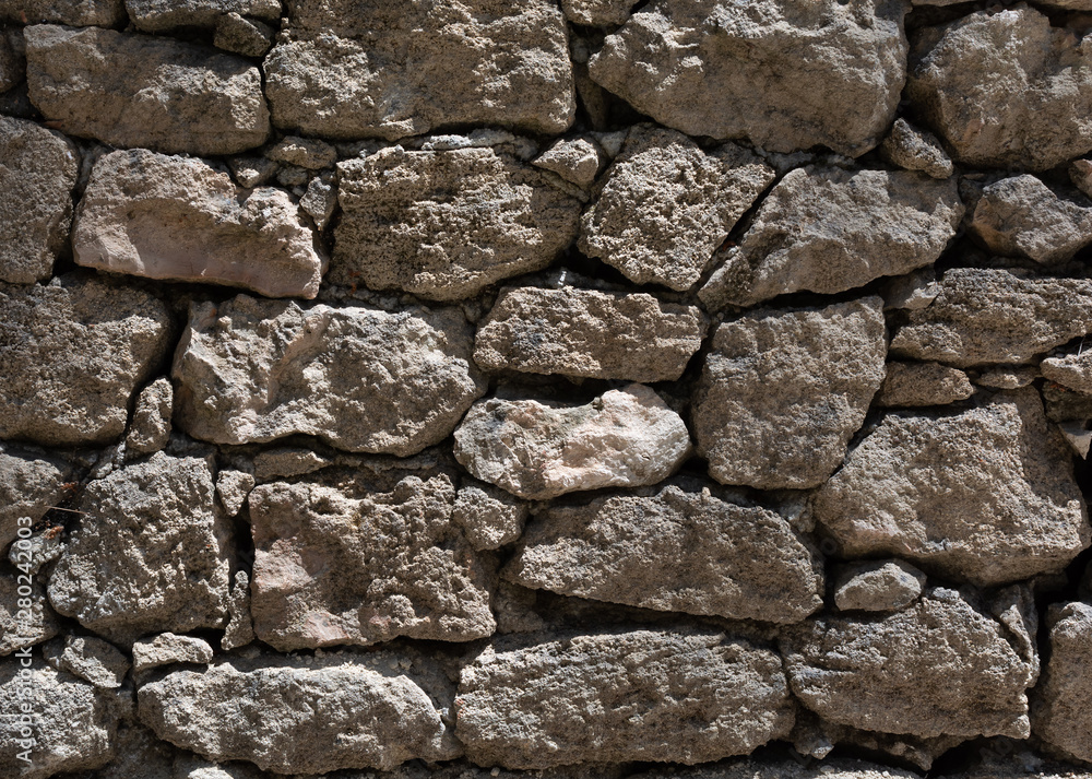 Fototapeta premium Grey stone wall texture with bright sunlight. Closeup