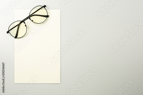 blank note paper and glasses on grey desk background.