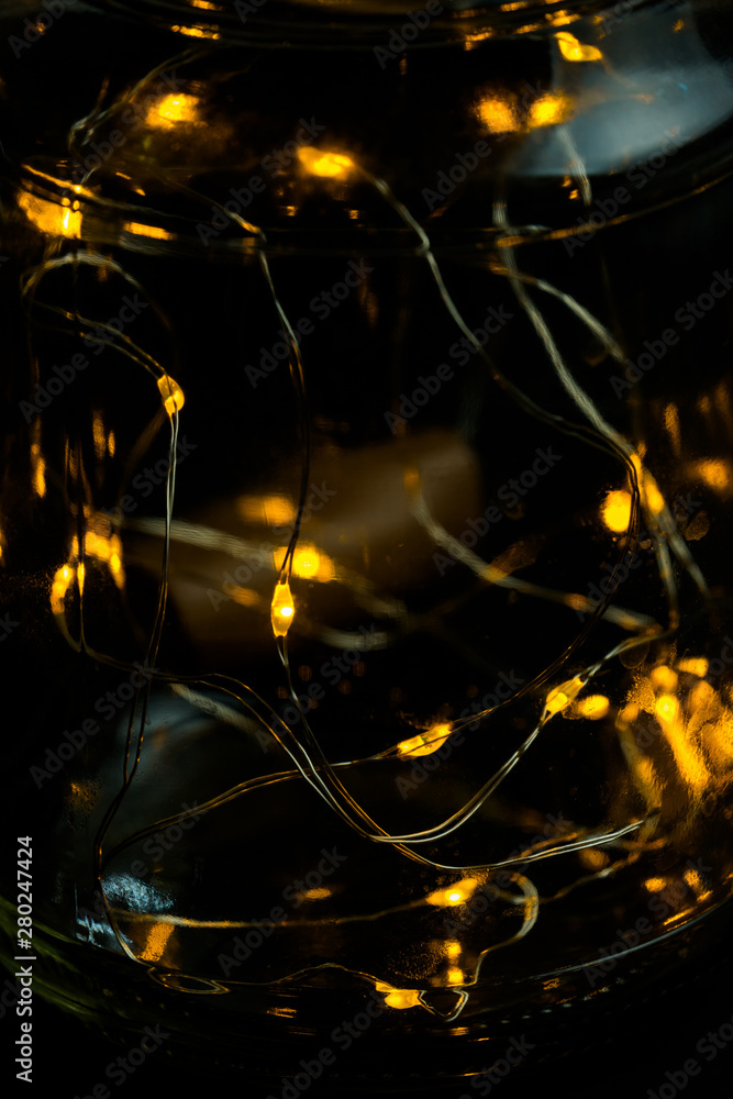 Decorative lights in glass jar at the dark room with mirror effect on dark background. Festive decorations .Warm white led lights.