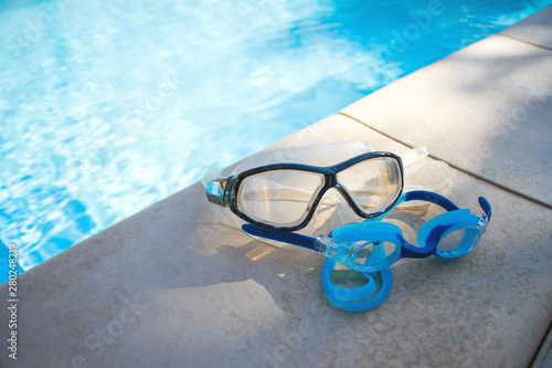 Two blue goggles for swimming lie on the side of the swimming pool on the background of crystal clear water