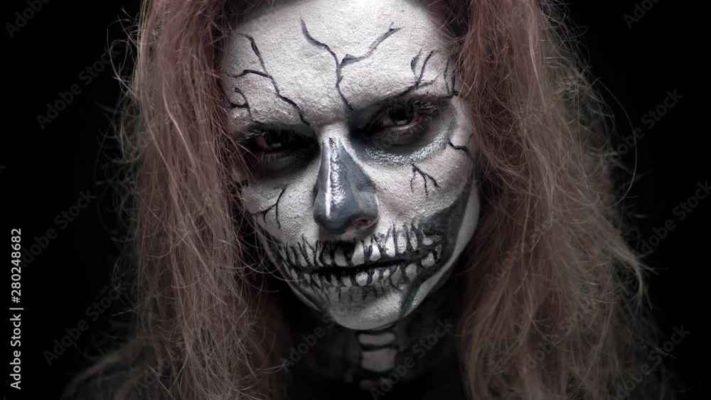 concept, beautiful makeup for halloween. Portrait of a young sexy girl with skull makeup. on a black background, face in the dark. close-up concept, beautiful makeup for halloween. Portrait of a young sexy girl with skull makeup. on a black background, face in the dark. close-up