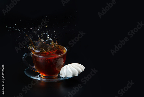 A cup of black tea on a black isolated background. Meringue next to the cup. Testy dessert. Splash