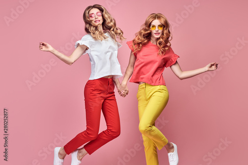 Two easy-going happy hipster Woman dance Fun in Stylish fashion colored red yellow pants. Beautiful excited Girl in summer Trendy outfit, sneakers jump laughing. Creative dancing fashionable concept