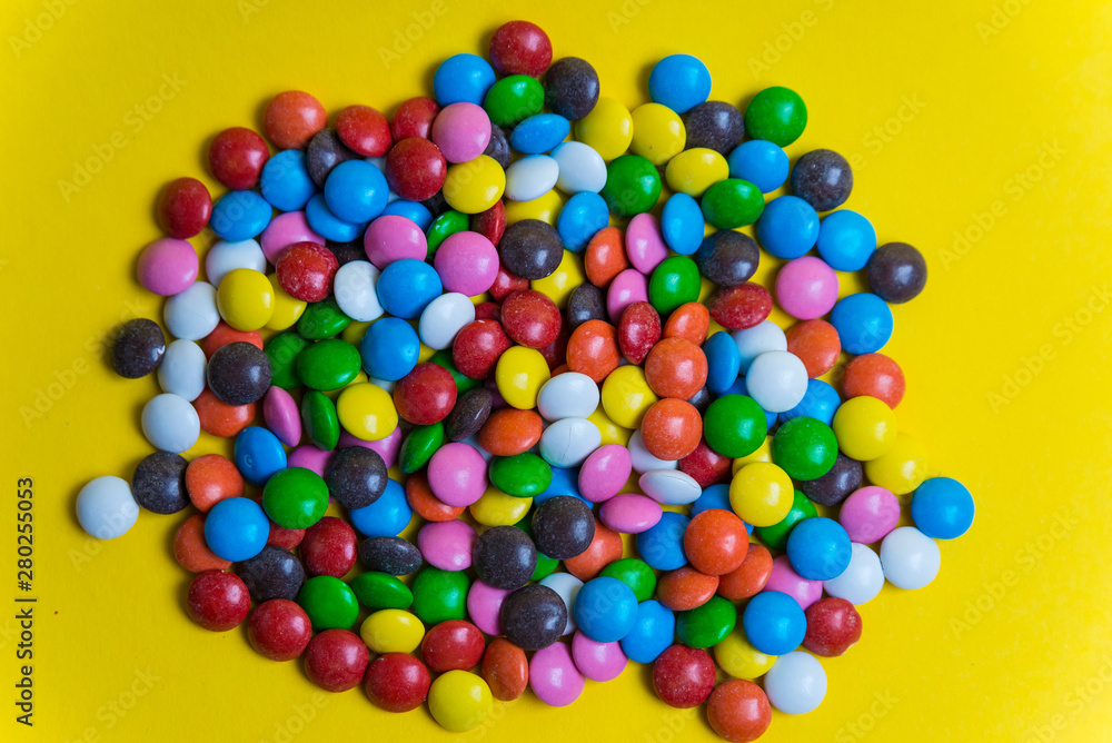 Obraz premium Colorful background of multicolored candy dragees. Round scattered sweets on a yellow bright background. Happy multicolor texture. Sweet candy wallpaper. Shallow depth of field. Flat lay on surface