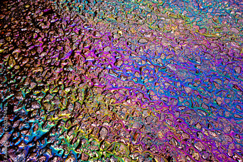 A leaked Car Oil Petrol in The Rain on a Tarmac Road Metallic Rainbow