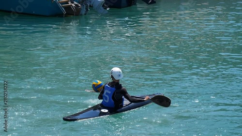 Single sportsman wearing buoyancy aid, helmet and face guard in kayak is practicing ball handling using paddle for canoe polo game. photo