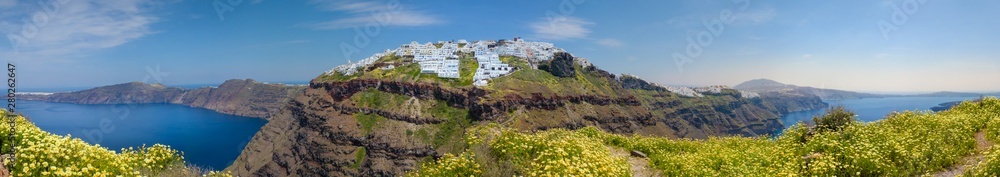 Santorini flower path, in front of the Imerovigli village, behind the city of Fira, with yellow daisies, typical for this greek isle in spring and a sunset in a similar color tone.