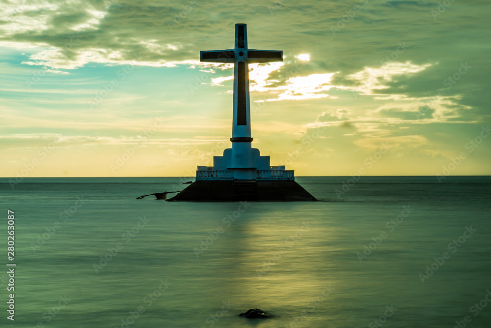 Sunset behind a large cross marking an old, sunken cemetery under the tropical ocean (Camiguin, Philippines)