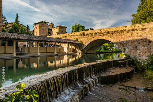 The ancient wash-house and the masonry bridge over the river, in the medieval village of Bevagna. Perugia, Umbria, Italy. Blue sky at sunset. Trees and vegetation. The reflection on the water surface.