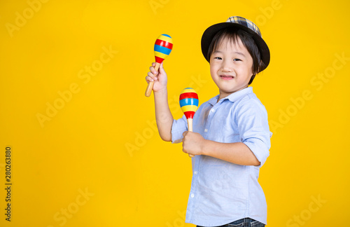 Portrait of little cute asian boy playing the maracas isolated on yellow background, preschool play group, music learning by doing and education concept photo