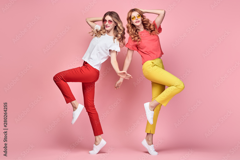 Two easy-going happy hipster Woman dance Fun in Stylish fashion colored red yellow pants. Beautiful excited Girl in summer Trendy outfit, sneakers jump laughing. Creative dancing fashionable concept Two easy-going happy hipster Woman dance Fun in Stylish fashion colored red yellow pants. Beautiful excited Girl in summer Trendy outfit, sneakers jump laughing. Creative dancing fashionable concept