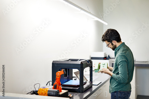 Side view of businessman examining model while standing by 3D printer in office photo