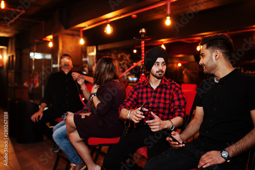 Group of indian friends sitting at lounge bar, smoke hookah and having rest.