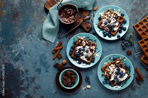 Chocolate belgian waffles with ice cream and fresh blueberry on blue background, top view