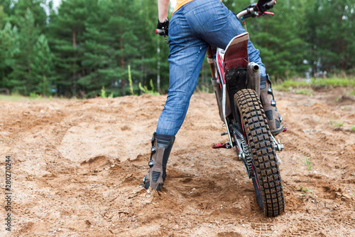 Adult man riding on sandy dirt track with his motorcross motorcycle, rear view, copyspace photo