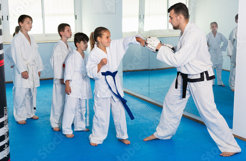Children training karate kicks on punching bag during karate class