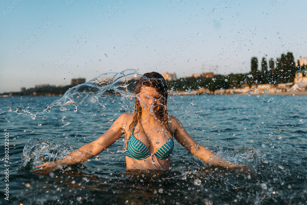 Fototapeta premium young beautiful girl resting on the ocean, jumping in the water, waving her arms, a lot of spray around her